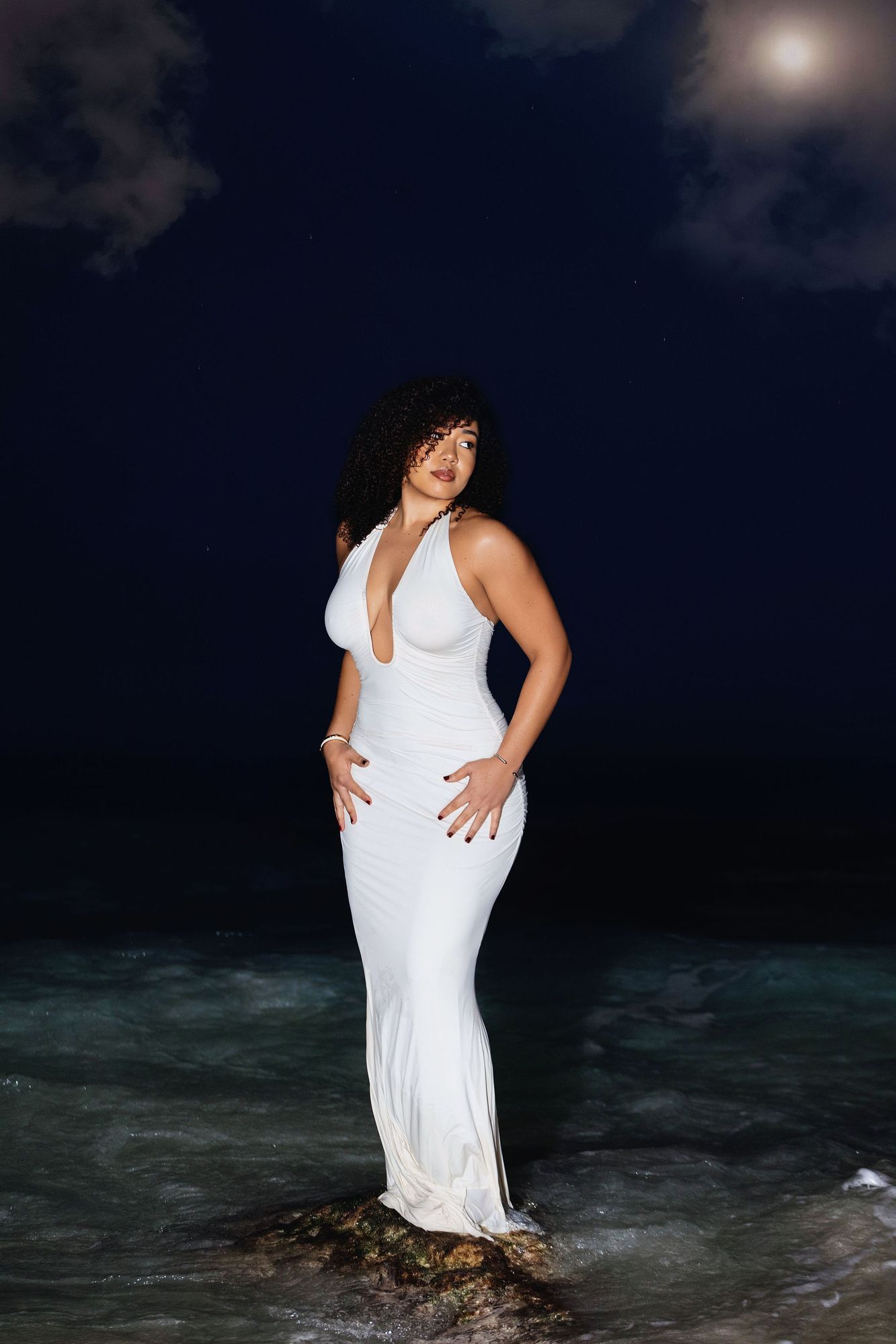 Woman in a white gown standing in the surf at night
